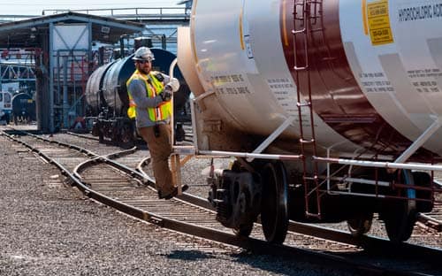 Image of rail switch operator riding tank car in railyard